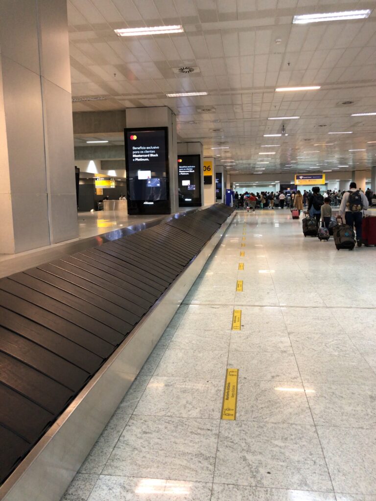ブラジル・グアルーリョス空港のターンテーブルで荷物を受け取る旅行者の様子