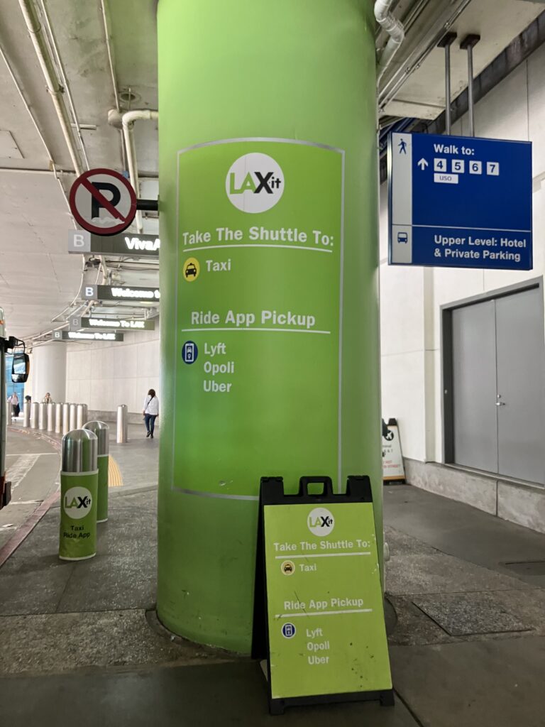 LAX空港ターミナル外にある緑色の「LAX-it」案内柱。Uber・Lyft・Opoliなどのライドシェア乗り場へ向かうシャトル案内が記載されたサイン。