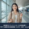 空港でクレジットカードを持って微笑む日本人女性。海外旅行に必要なカードを3枚持って準備している様子。