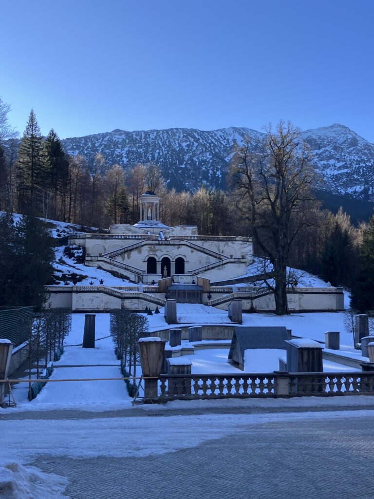 冬のリンダーホーフ城の庭園。雪に覆われた庭と背後に広がるアルプスの山々